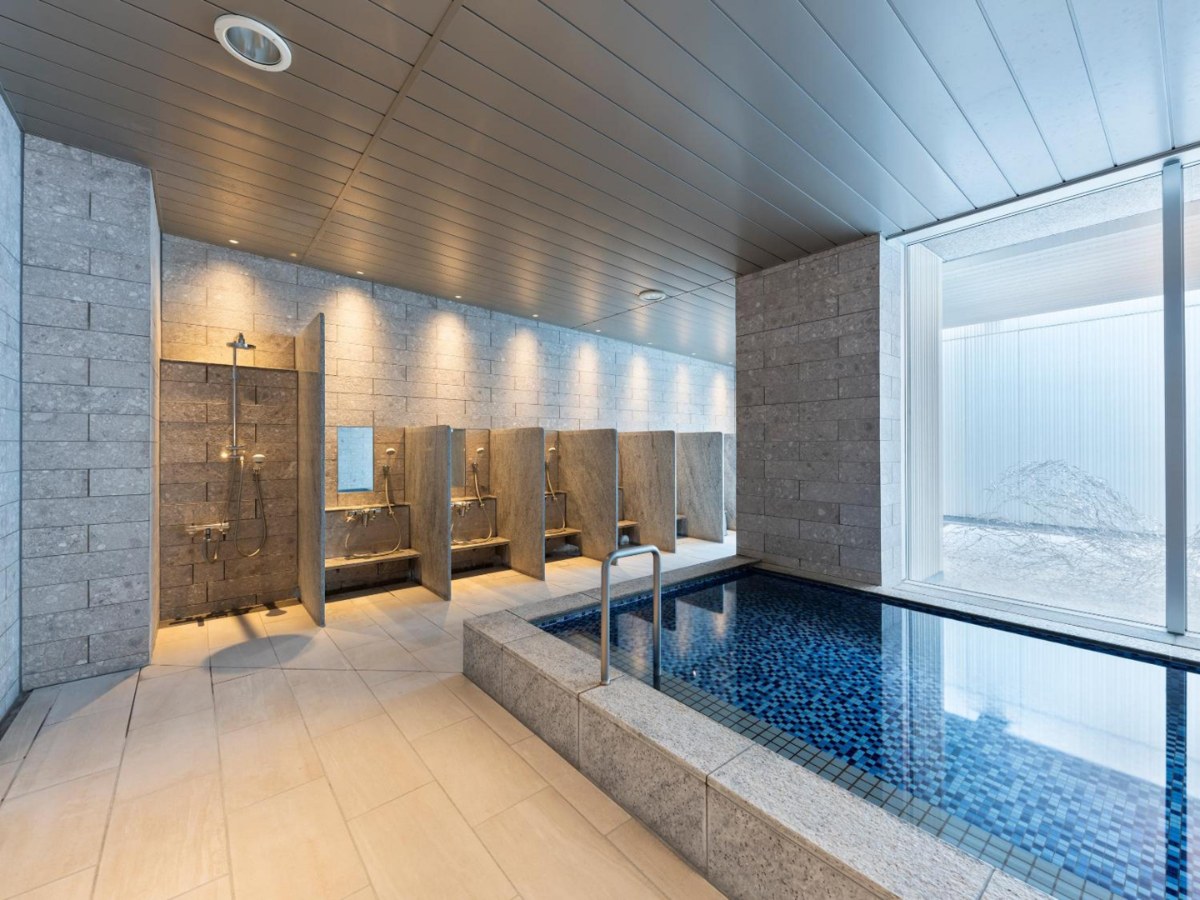 Blue-tiled public bath beside a bright courtyard window at Mitsui Garden Hotel Nagoya Premier