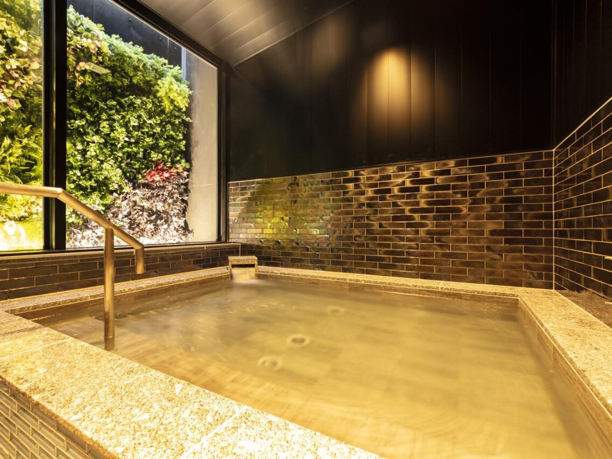 Stone-edged spa bath with a garden window and dark tiled walls at Sanco Inn Grande Nagoya