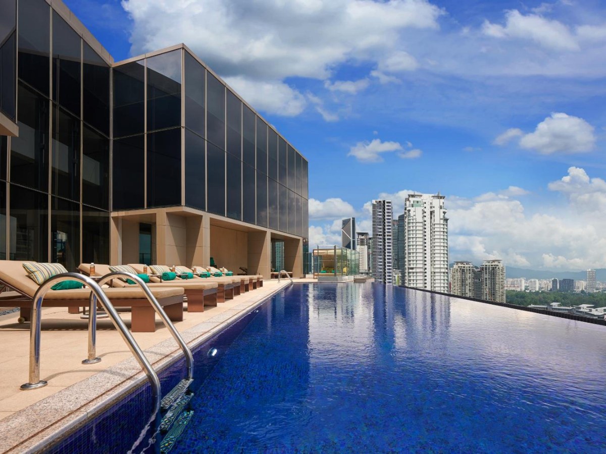 Rooftop infinity pool with loungers under a blue sky at Pavilion Hotel Kuala Lumpur
