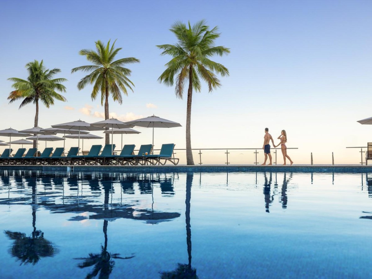 Infinity pool with loungers and palm trees at dusk at Cozumel Palace