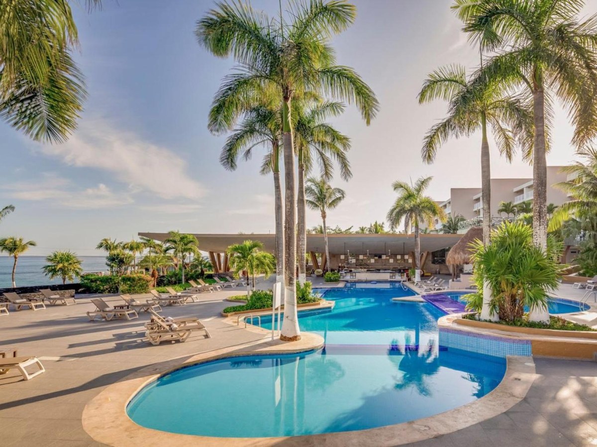 Curved pool with loungers and palm trees at Fiesta Americana Cozumel