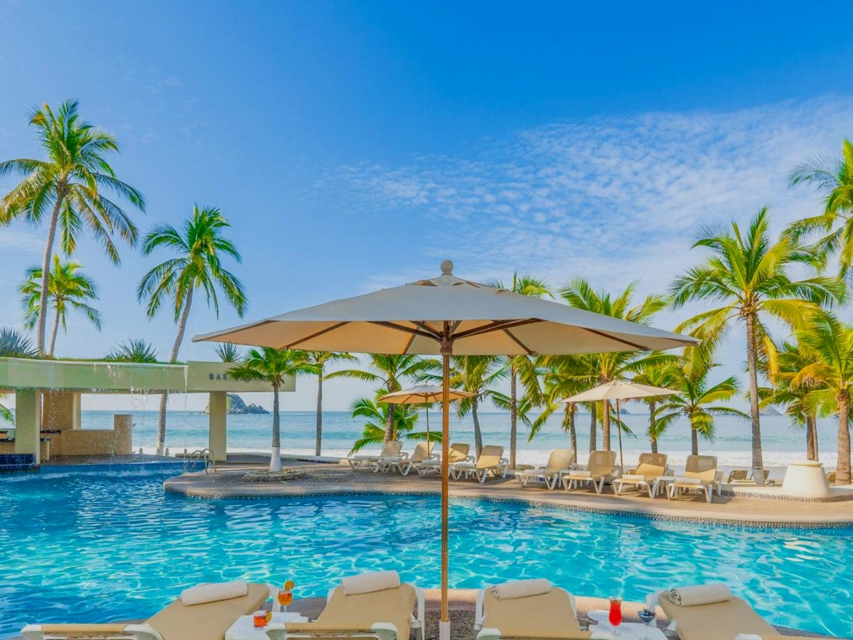 Resort swimming pool with chairs and palm trees at Barceló Ixtapa All Inclusive