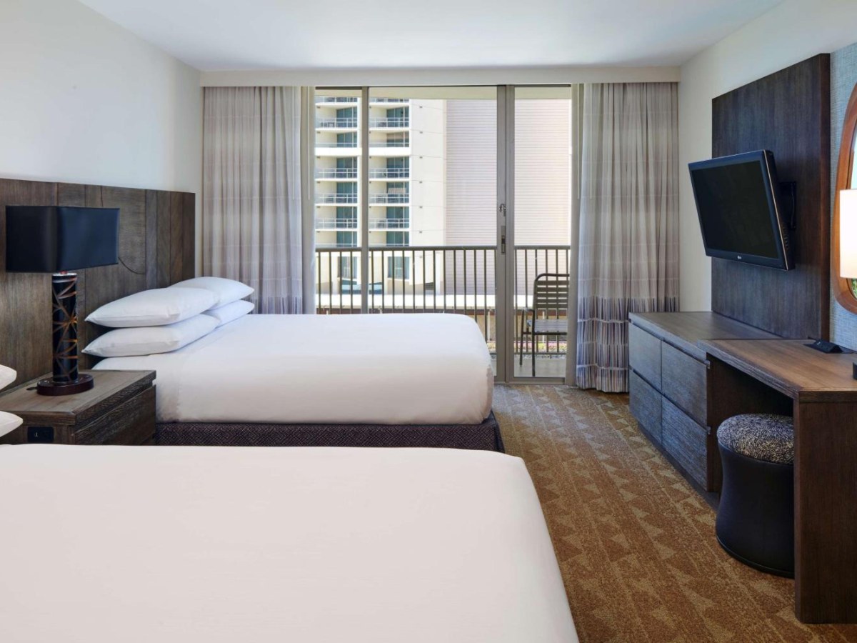 Two large double beds and a balcony view in an Embassy Suites Waikiki Beach Walk queen suite